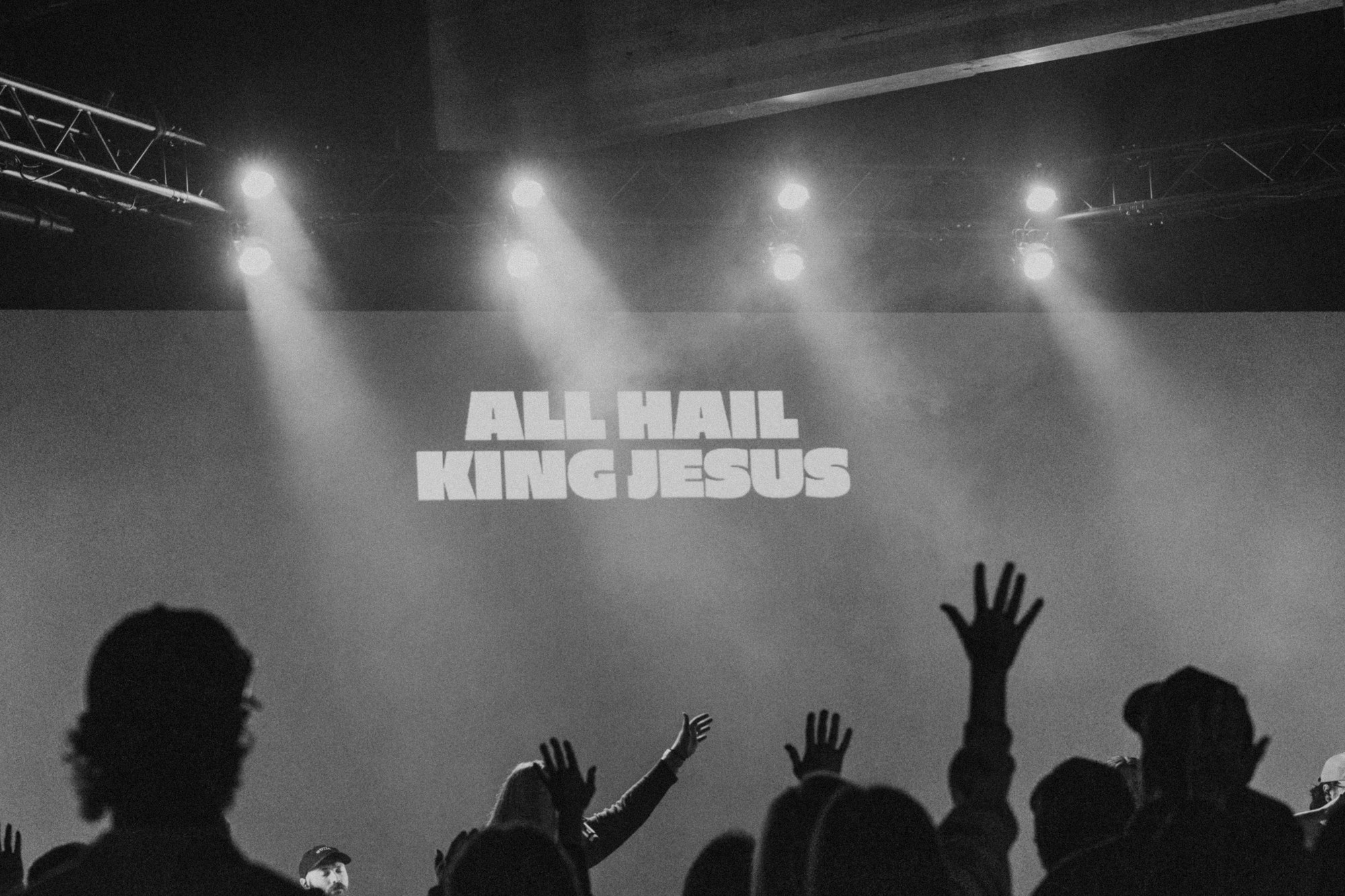 People at Rise raising their hands in worship beneath the words All Hail King Jesus